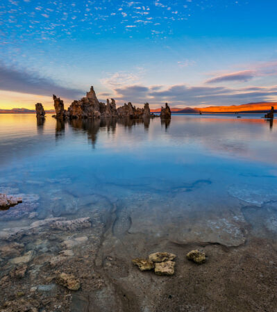 This photograph captures a tranquil and breathtaking scene of Mono Lake lake with tufas emerging from the water. The water reflects the vibrant hues of the sunset, while the clouds create a dynamic pattern. In the distance, the Sierra Nevada mountains project their silhouettes against the colorful sky.