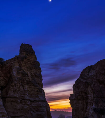 The image beautifully blends the majesty of natural geological features with the subtle elegance of celestial and atmospheric transitions. Dominating the foreground are two imposing rock formations that frame Praia da Rocha beach. The last color left from the setting sun contrasts with the deep blue dark sky, adding depth and mood to the scene.