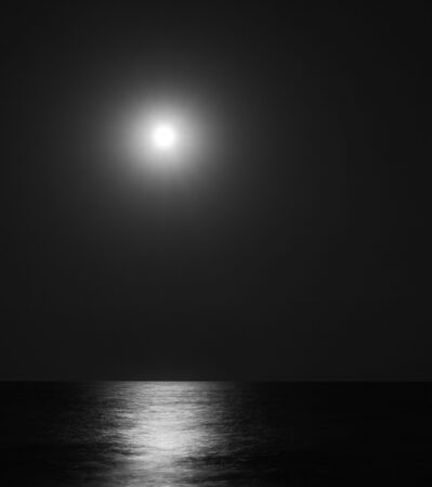 A luminous full moon casts a bright, diffused glow across the dark sky and creates a reflective pathway on the calm surface of the Black Sea, which occupies the lower half of the photograph. The interplay of light and shadow evokes a sense of tranquility and solitude.