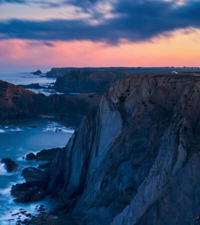 The towering cliffs that sharply drop into the restless sea seem even more dramatic after a spring storm. The rocky coastline of the Algarve at Arrifana, laden with craggy outcrops, extends into the distance, creating a sense of depth and vastness.
