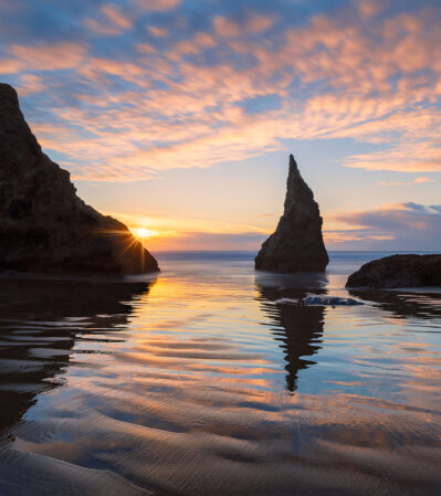 The soft, golden glow of the sunset at Bandon Beach, Oregon and the interplay between light and shadow create a dynamic and captivating visual spectacle captured beautifully in this image.